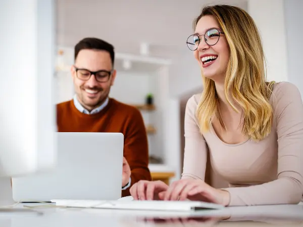 Nainen ja mies istuvat pöydän ääressä ja työskentelevät tietokoneilla