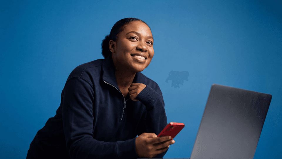 woman smiling holding phone in front of laptop
